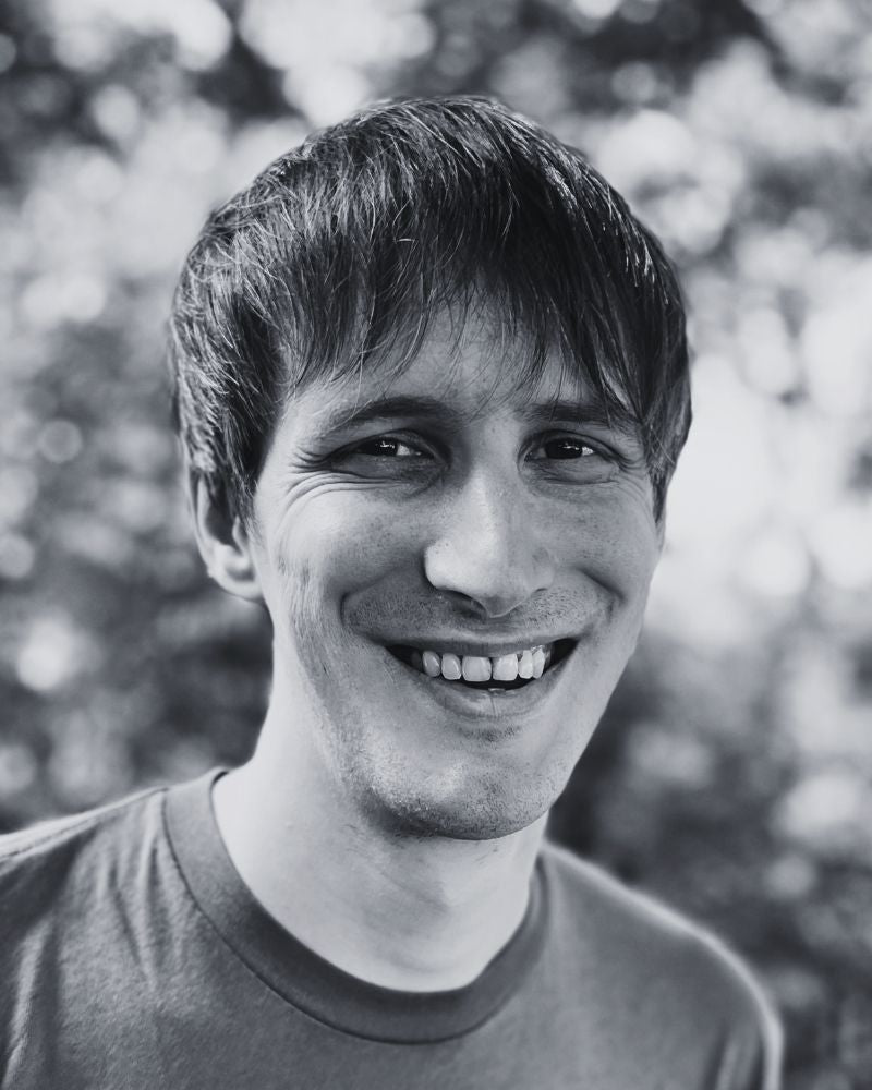 Black and white photo of a smiling person outdoors with trees in the background