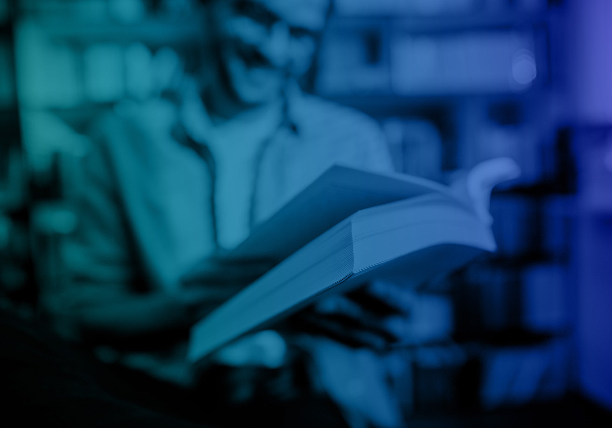 A person in a library or study holding and reading an open book, captured in a moody blue and teal-toned photograph.