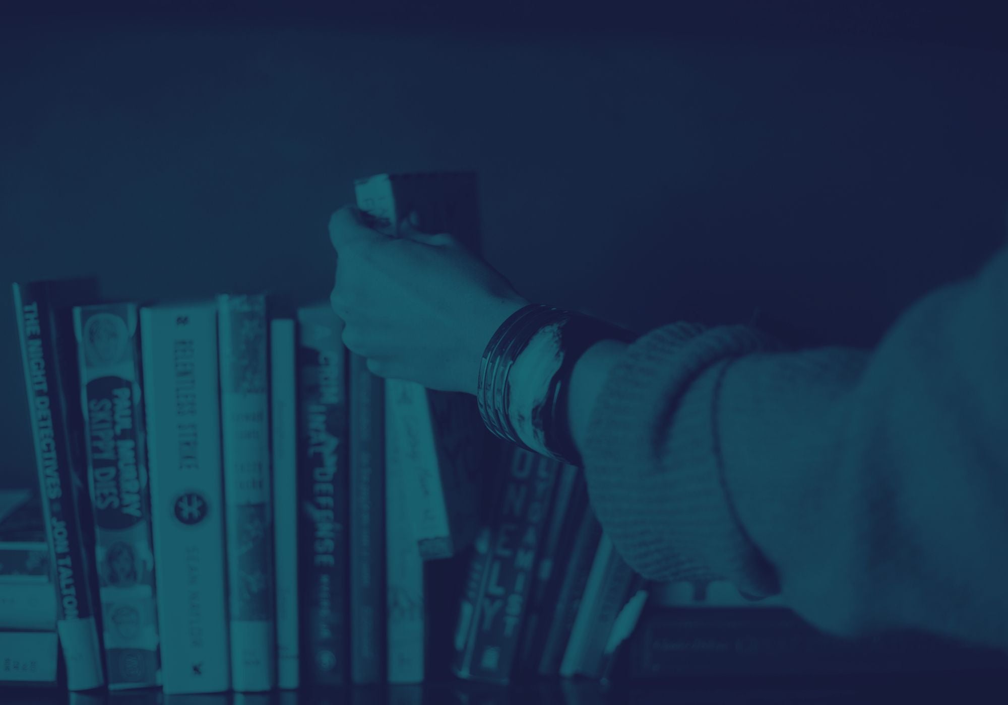 Person's hand reaching towards a stack of books with a blue filter