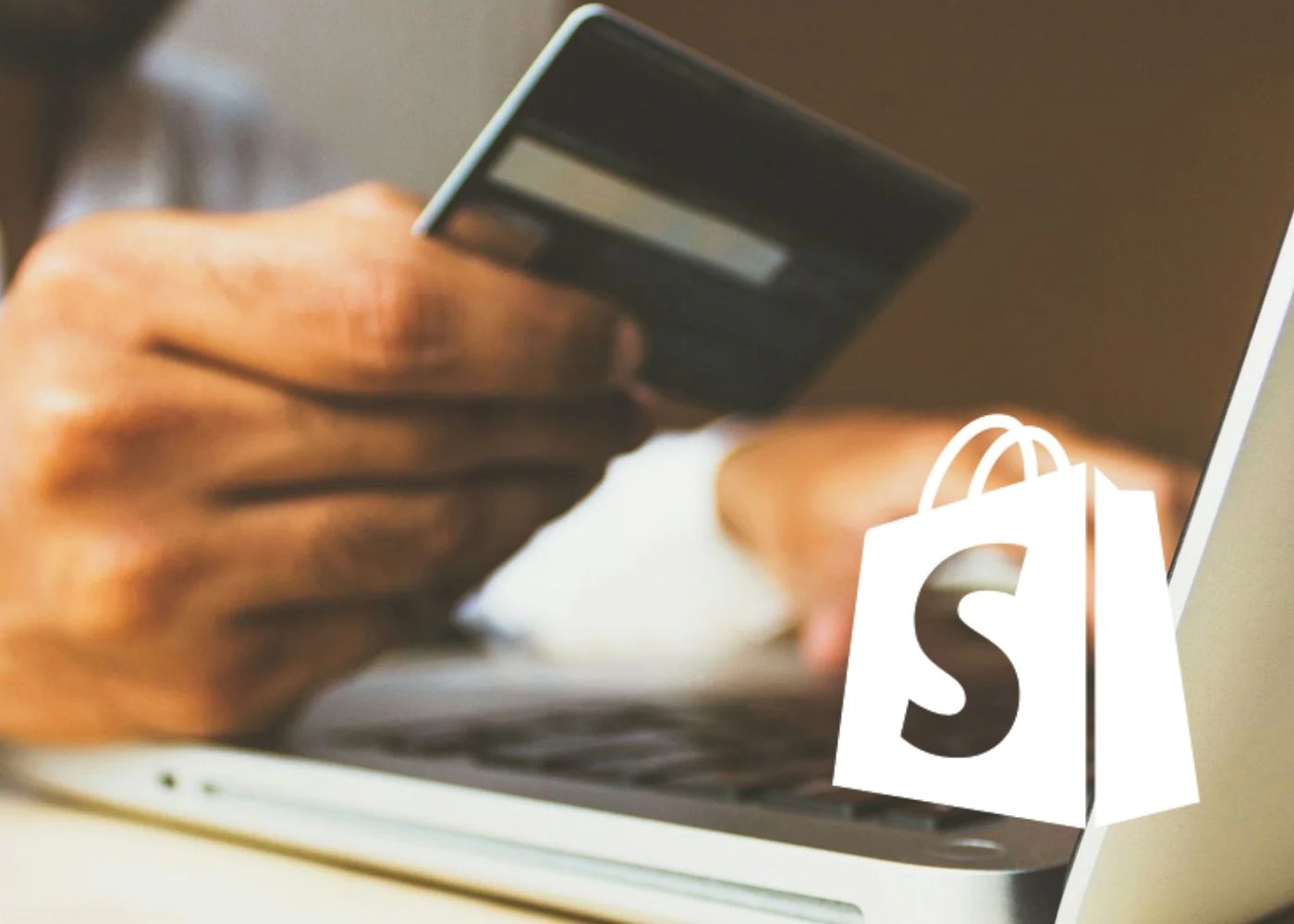 Person holding a credit card over a laptop with a Shopify logo overlay.