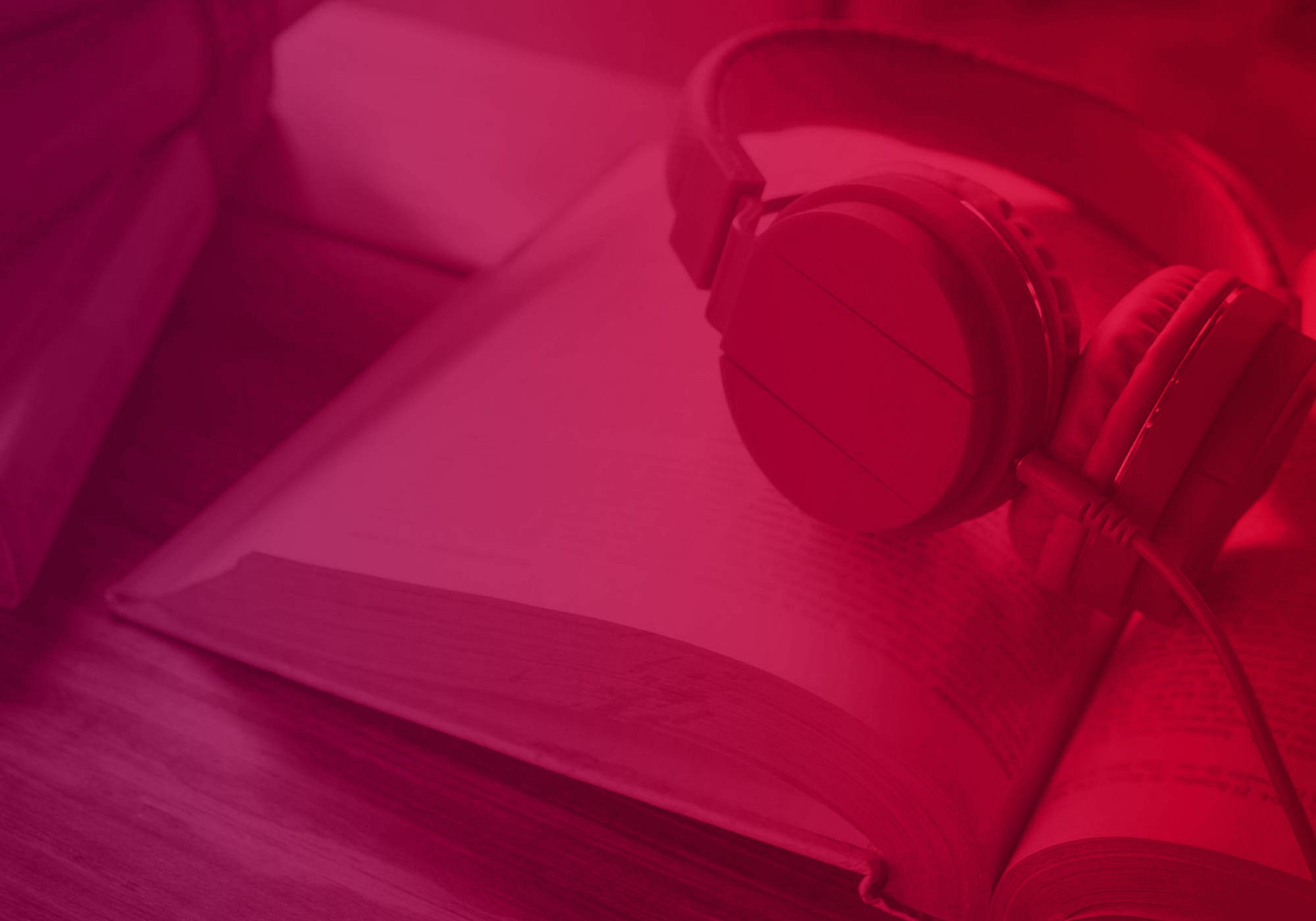 Over-ear headphones resting on an open book, bathed in a strong red light tint.