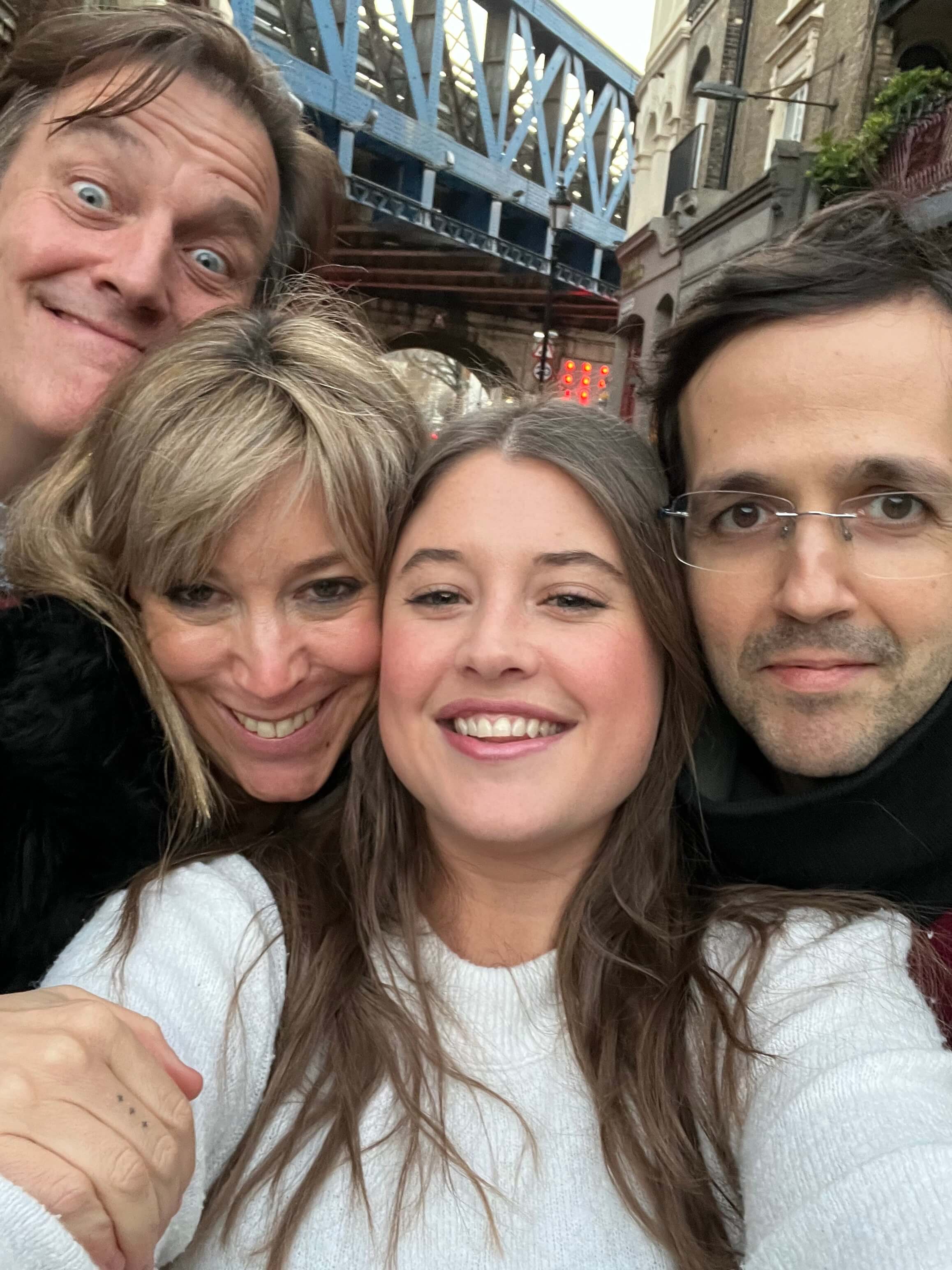 Four people posing for a selfie with a bridge and cityscape in the background