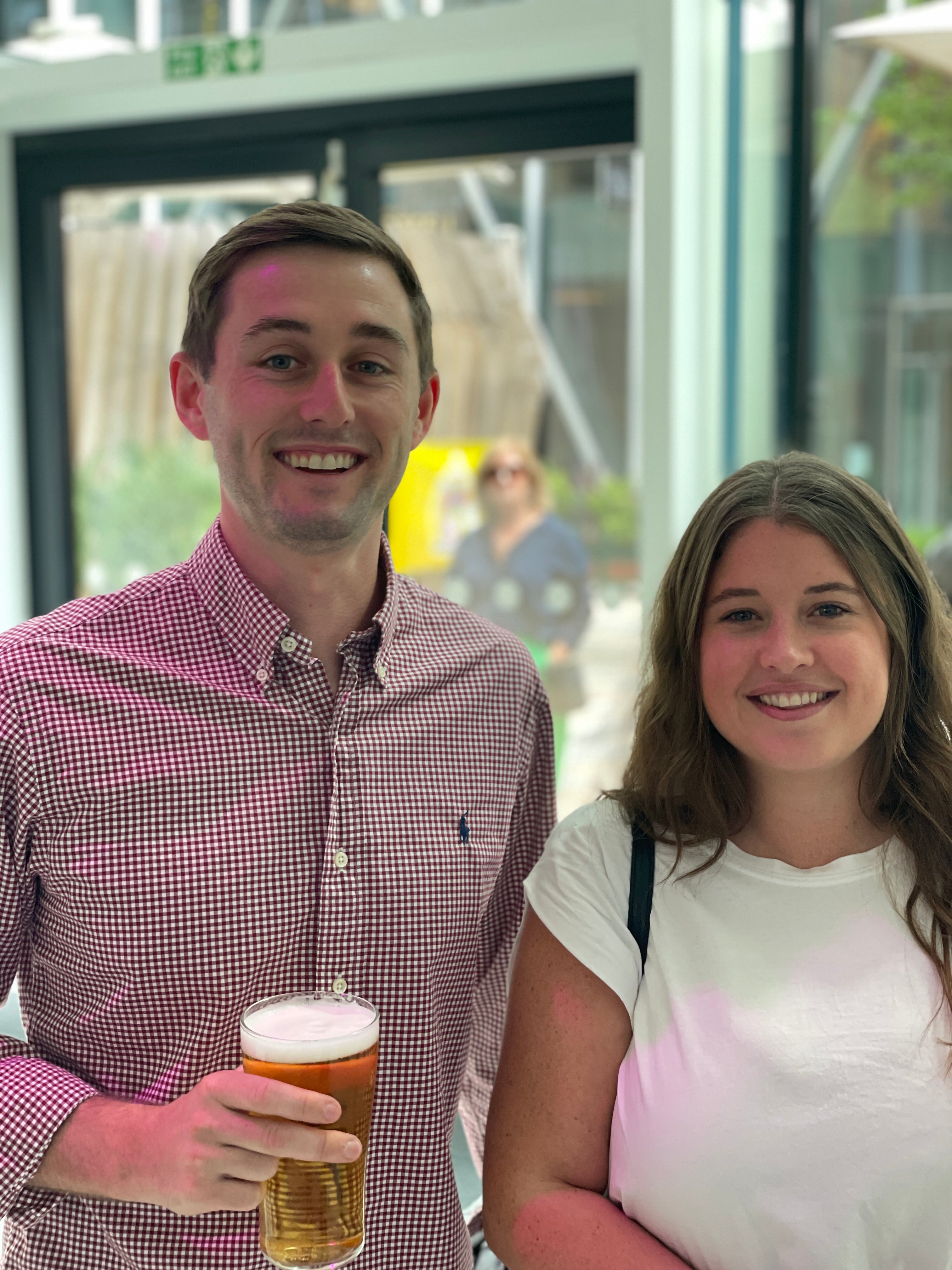 Two people standing together, one holding a beer, in an outdoor building reception setting.