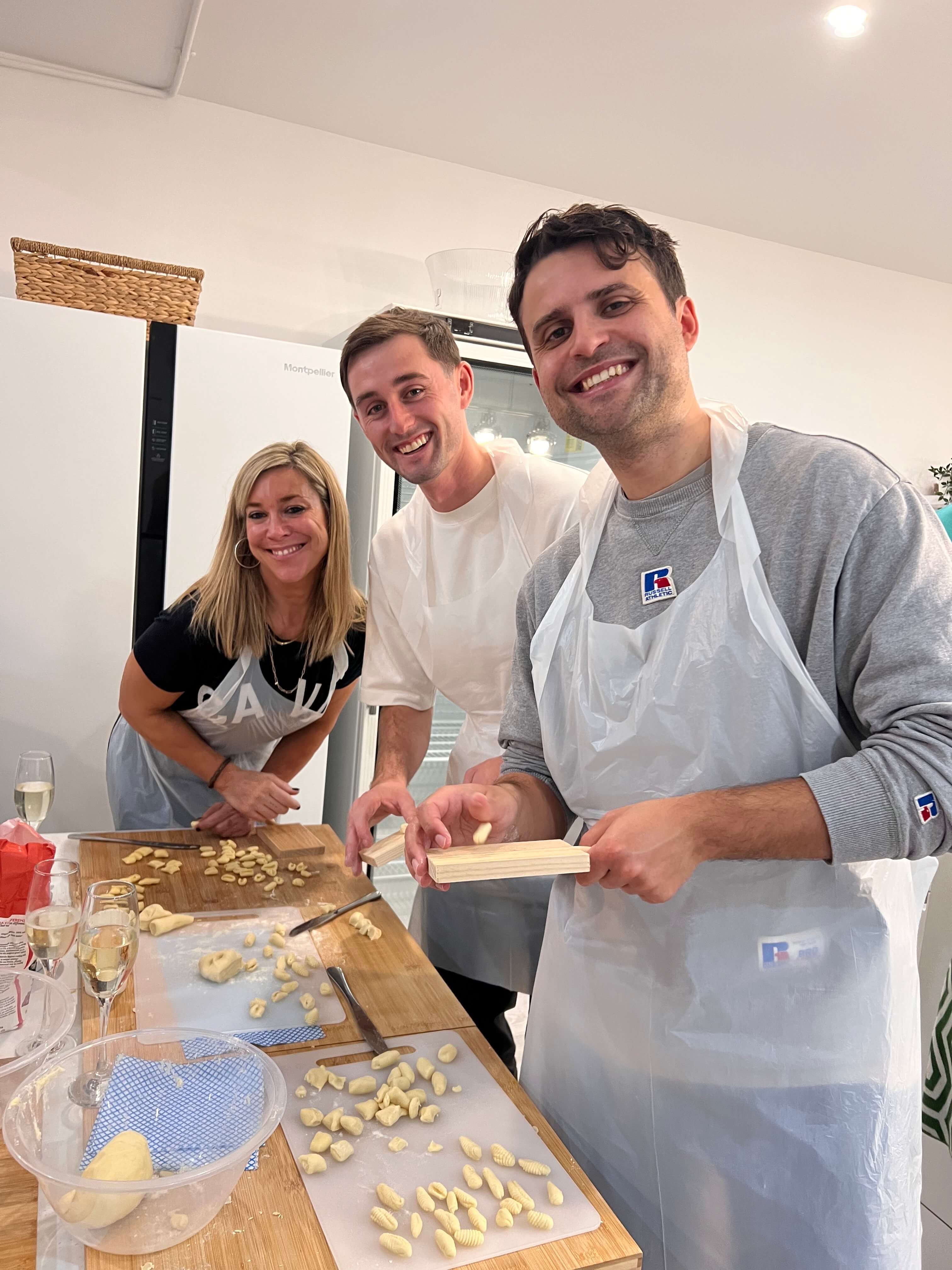 Three people in a kitchen preparing food, wearing aprons.