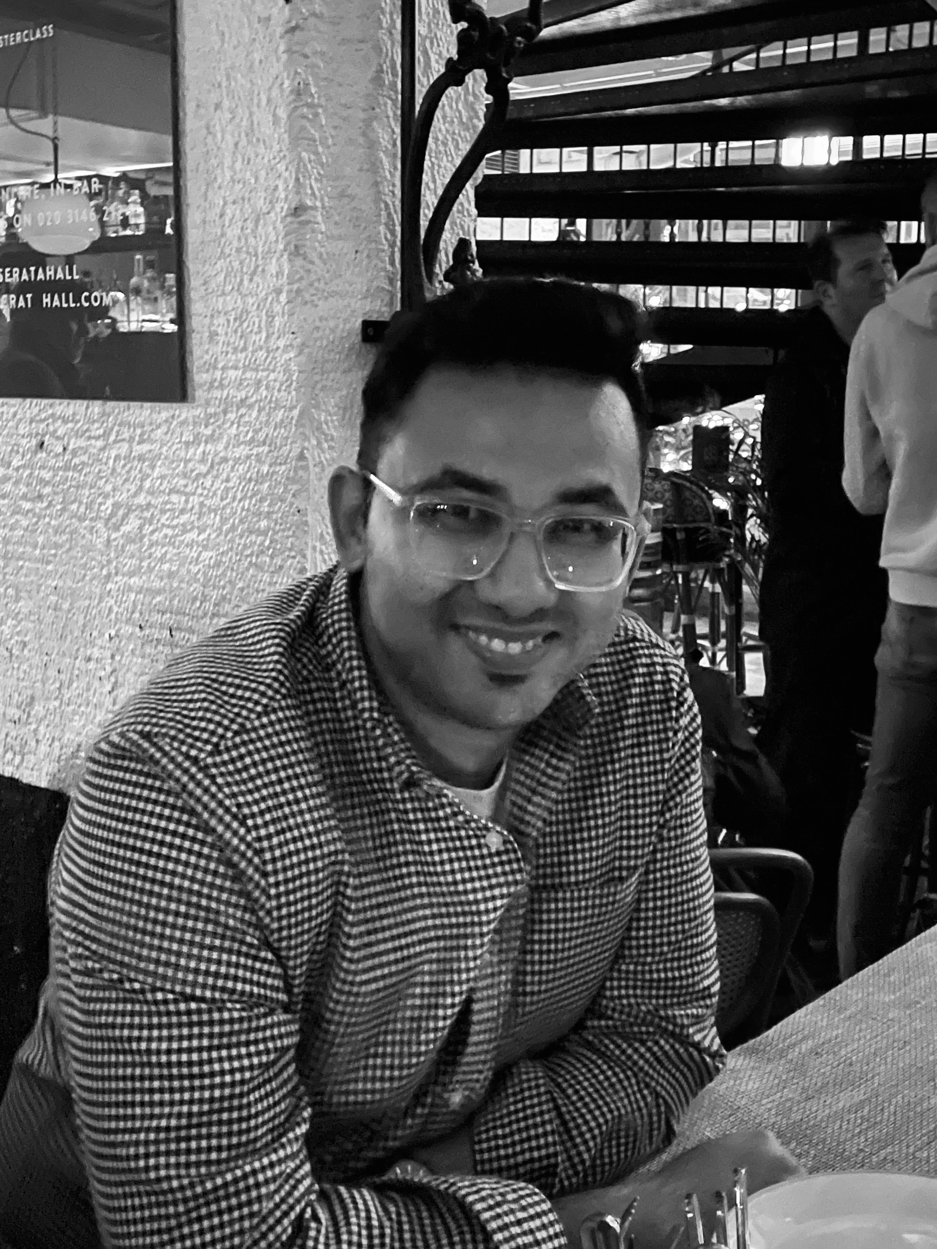 Man wearing glasses and a checkered shirt sitting at a table in a casual setting.