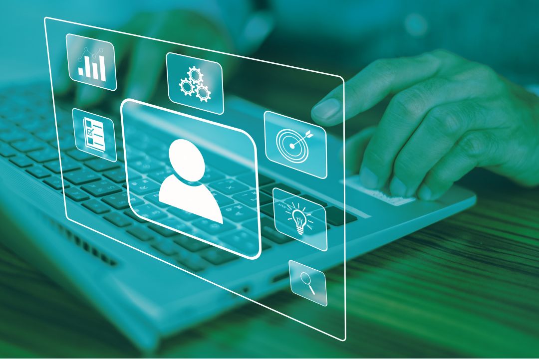 A person's hand typing on a laptop keyboard, overlaid with a translucent digital interface showing user profile, settings, charts, and target icons in a teal-green tinted scene.