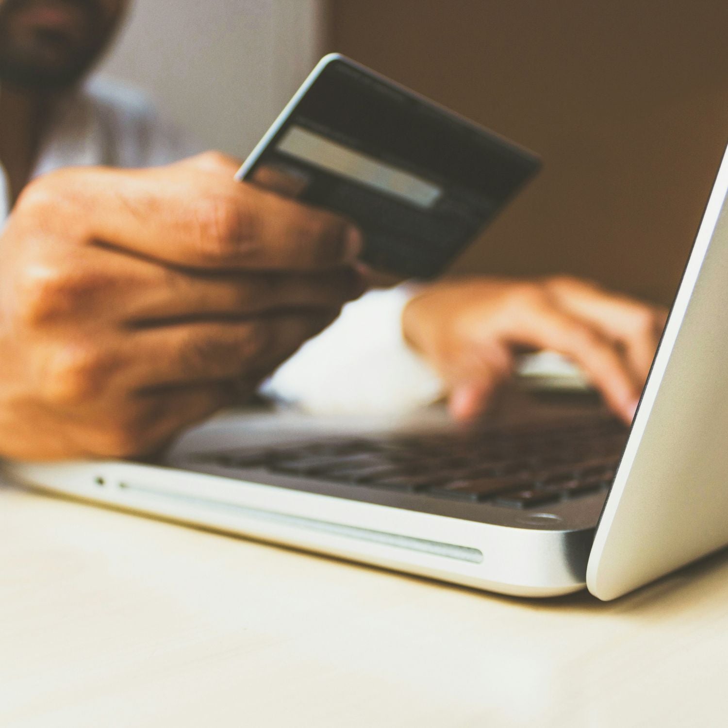 Person holding a credit card and using a laptop on a table.