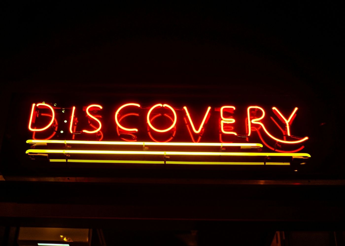 A photo of an orange and yellow neon sign in the dark that reads discovery