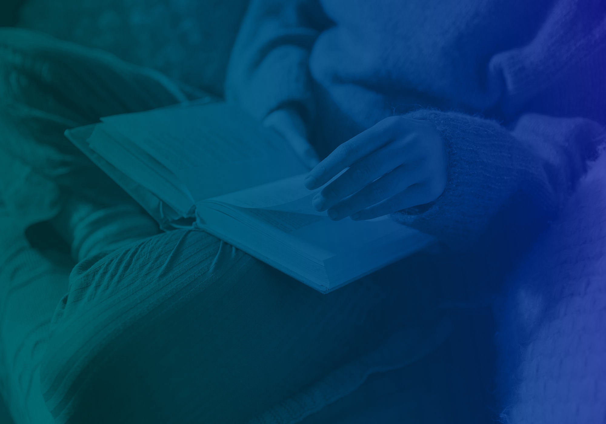 A person in a cozy knit sweater holds an open book or notebook, captured in a moody blue and teal-lit setting.